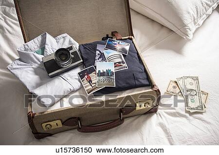 Stock Image - Open suitcase on bed with camera and photographs. Fotosearch