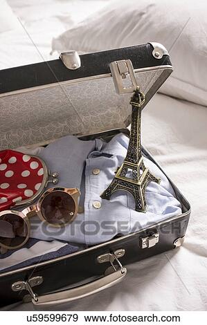 Stock Photo - Open suitcase on bed with eiffel tower souvenir and sunglasses. Fotosearch