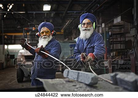 Stock Image - Operatives dragging newly heat treated forgings off trays and into steel container in heat treatment area. Fotosearch