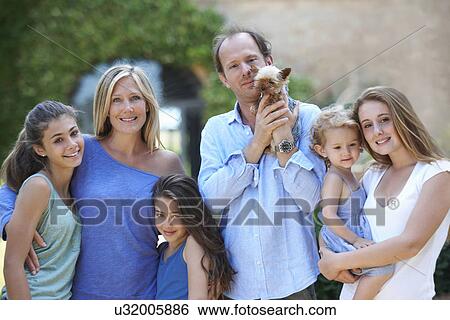 Stock Photograph - Parents standing with daughters and dog in garden. Fotosearch