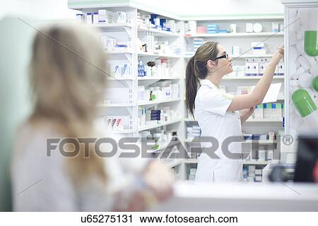 Stock Image - Pharmacist getting medication from shelf. Fotosearch