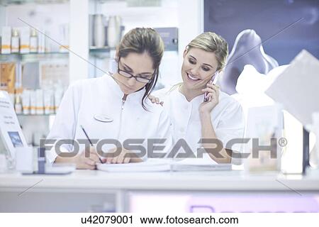 Pharmacists at desk, one on phone call and one writing paperwork View Large Photo Image Stock Image - Pharmacists at desk, one on phone call and one writing paperwork. Fotosearch