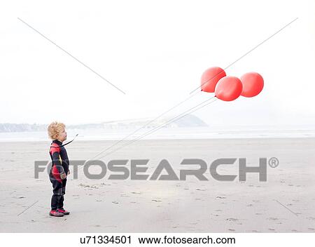 Stock Image - Portrait of boy on beach with red balloons. Fotosearch