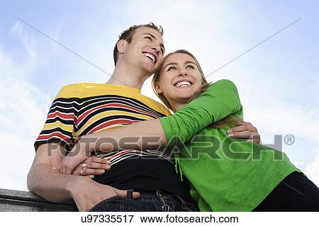 Stock Photo - Portrait of couple with arms around each other smiling. Fotosearch