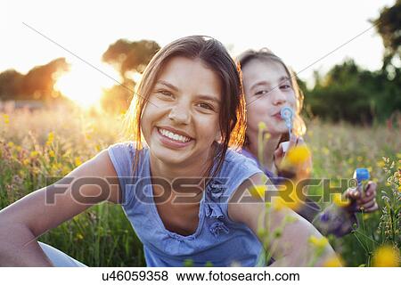 Portrait of girls sitting in field, one blowing bubbles View Large Photo Image Stock Photo - Portrait of girls sitting in field, one blowing bubbles. Fotosearch