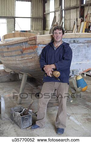 Stock Image - Portrait of mature man holding chisel in boat workshop. Fotosearch