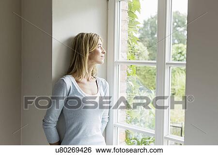 Stock Photograph - Portrait of mid adult woman looking out of window. Fotosearch