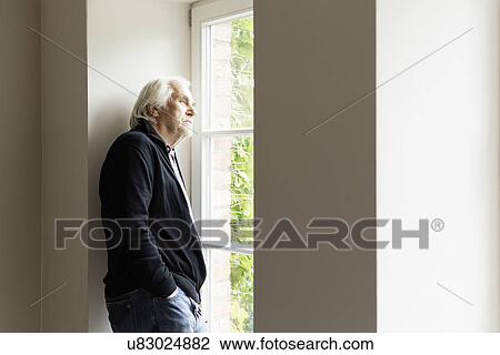 Stock Image - Portrait of senior man looking out of window. Fotosearch