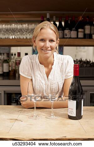 Picture - Portrait of waitress with wine bottle and glasses at kitchen counter. Fotosearch