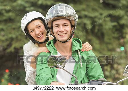 Stock Image - Portrait of young couple in helmets sitting on vespa. Fotosearch