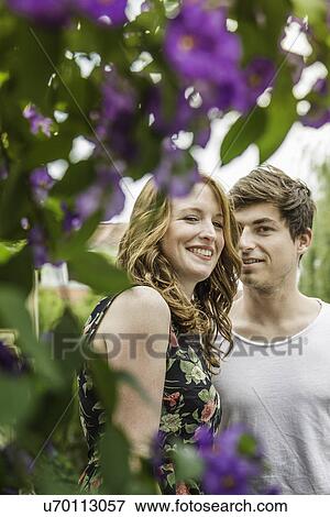 Stock Photo - Portrait of young couple surrounded by foliage and flowers. Fotosearch