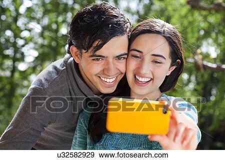Stock Photo - Portrait of young couple taking self portrait in garden. Fotosearch