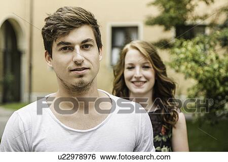 Portrait of young man with girlfriend standing in background View Large Photo Image Stock Photograph - Portrait of young man with girlfriend standing in background. Fotosearch