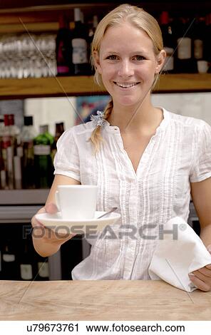 Portrait of young waitress holding coffee at kitchen counter View Large Photo Image Stock Image - Portrait of young waitress holding coffee at kitchen counter. Fotosearch