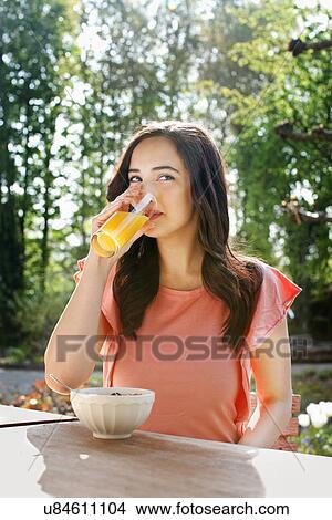 Picture - Portrait of young woman drinking orange juice in garden. Fotosearch