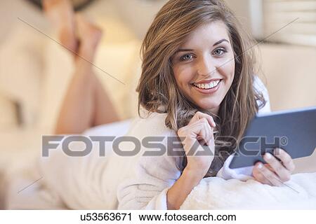 Stock Image - Portrait of young woman lying on bed with digital tablet. Fotosearch