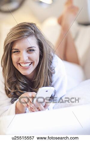 Portrait of young woman lying on bed with mobile phone View Large Photo Image Stock Photo - Portrait of young woman lying on bed with mobile phone. Fotosearch