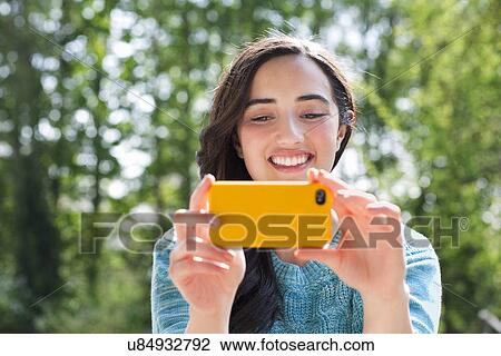 Stock Image - Portrait of young woman taking self portrait in garden. Fotosearch