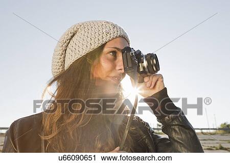 Stock Image - Portrait of young woman using slr camera. Fotosearch