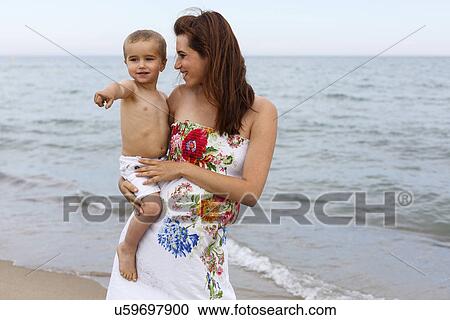 Stock Image - Pregnant woman holding toddler on beach. Fotosearch