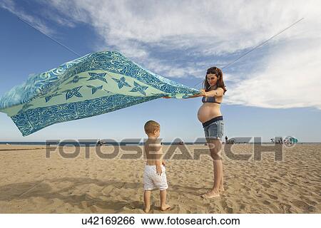 Stock Photograph - Pregnant woman on beach with blanket waving in wind. Fotosearch