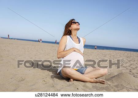 Picture - Pregnant woman sitting on beach. Fotosearch
