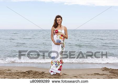 Pregnant woman standing on beach, hands on stomach View Large Photo Image Stock Photo - Pregnant woman standing on beach, hands on stomach. Fotosearch