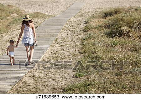 Stock Image - Rear view of mother and son walking down boardwalk to beach. Fotosearch