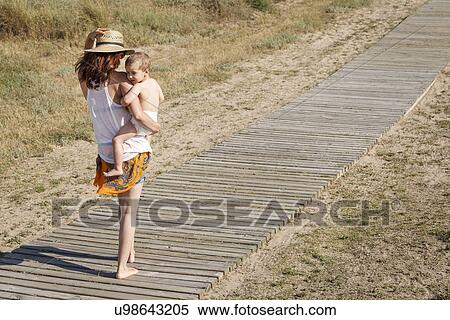 Rear view of mother walking down boardwalk carrying son in arms View Large Photo Image Stock Photography - Rear view of mother walking down boardwalk carrying son in arms. Fotosearch