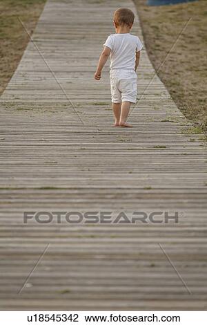 Stock Image - Rear view of toddler walking along boardwalk. Fotosearch