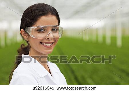 Stock Photography - Scientist wearing goggles in front of plants in greenhouse. Fotosearch
