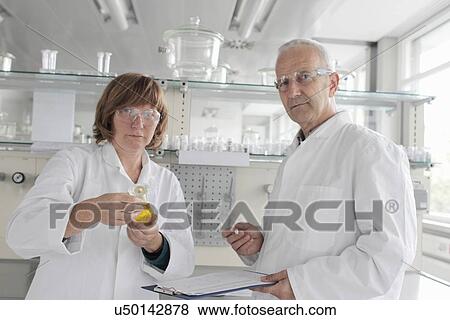 Scientists working in laboratory, holding yellow liquid in vial View Large Photo Image Stock Photo - Scientists working in laboratory, holding yellow liquid in vial. Fotosearch