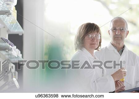 Stock Photo - Scientists working in laboratory, holding vial. Fotosearch