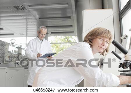 Scientists working in laboratory, woman with microscope and man taking notes View Large Photo Image Stock Photo - Scientists working in laboratory, woman with microscope and man taking notes. Fotosearch