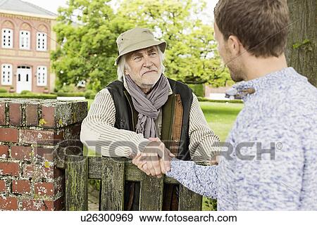 Stock Photo - Senior man and mid adult man shaking hands over gate. Fotosearch