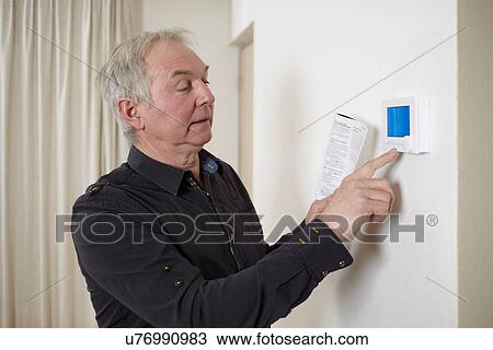 Stock Image - Senior man at home adjusting heating control panel. Fotosearch