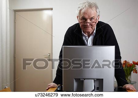 Senior man at home standing in front of personal comuter View Large Photo Image Stock Photo - Senior man at home standing in front of personal comuter. Fotosearch