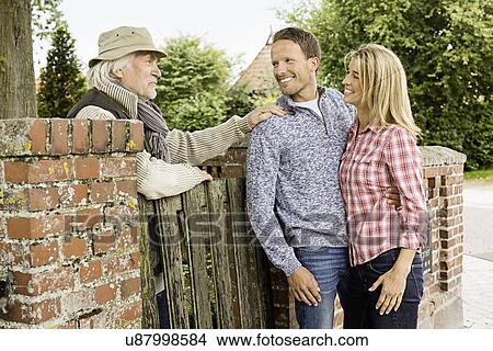Picture - Senior man leaning on gate talking to with mid adult couple. Fotosearch