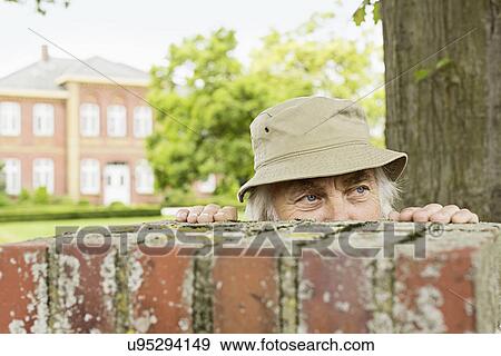 Senior man wearing hat peering over garden wall View Large Photo Image Stock Photo - Senior man wearing hat peering over garden wall. Fotosearch