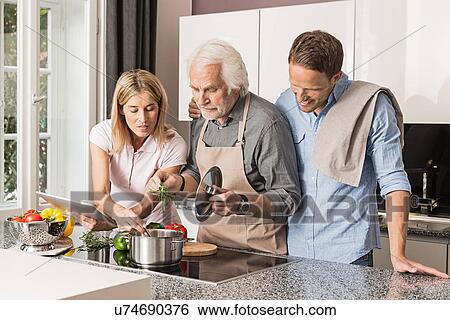 Stock Photograph - Senior man with mid adult couple preparing food. Fotosearch