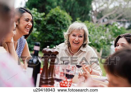Stock Image - Senior woman enjoying meal with family. Fotosearch