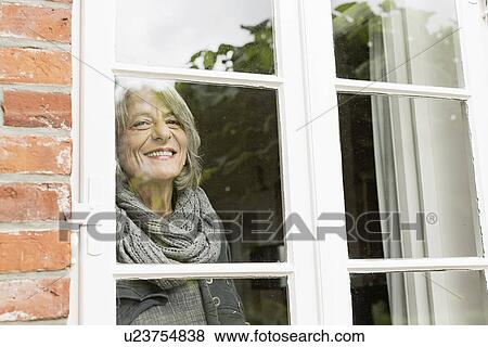Stock Photo - Senior woman looking through window. Fotosearch
