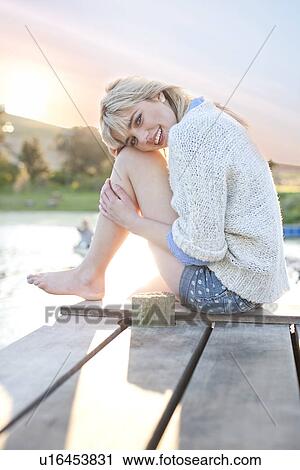 Stock Image - Shy young woman sitting on pier. Fotosearch