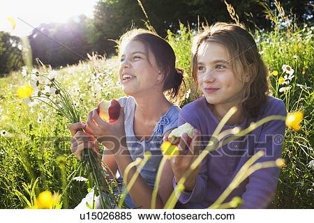 Stock Photography - Sisters sitting in field eating apples. Fotosearch