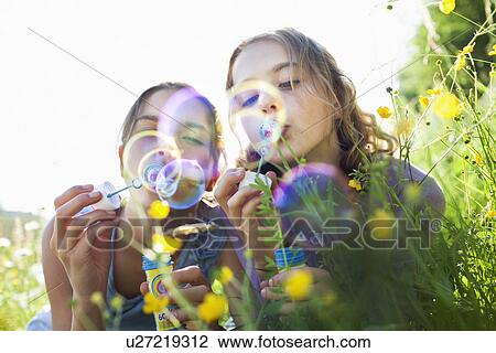 Sisters sitting in field of flower blowing bubbles View Large Photo Image Stock Image - Sisters sitting in field of flower blowing bubbles. Fotosearch