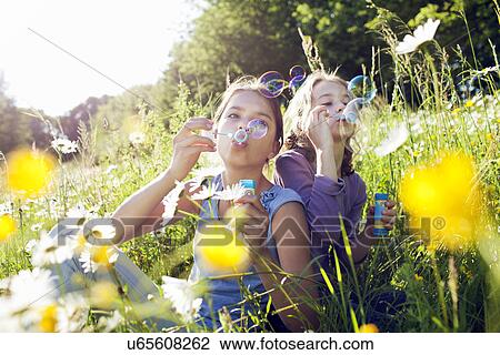 Sisters sitting in field of flower blowing bubbles View Large Photo Image Stock Image - Sisters sitting in field of flower blowing bubbles. Fotosearch