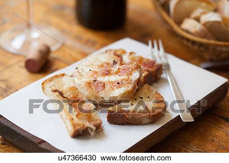 Stock Image - Still life of toasted bread with melted cheese on chopping board. Fotosearch