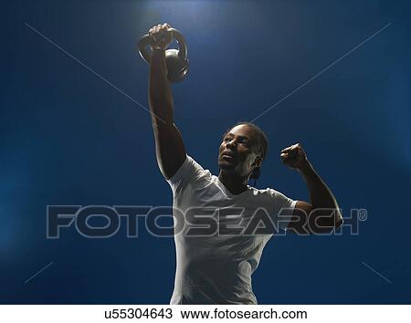 Stock Image - Studio portrait of young man holding up kettlebell. Fotosearch