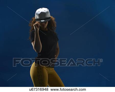 Studio portrait of young woman tipping her baseball cap View Large Photo Image Stock Photo - Studio portrait of young woman tipping her baseball cap. Fotosearch