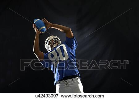 Stock Photo - Studio shot of american footballer reaching for ball. Fotosearch